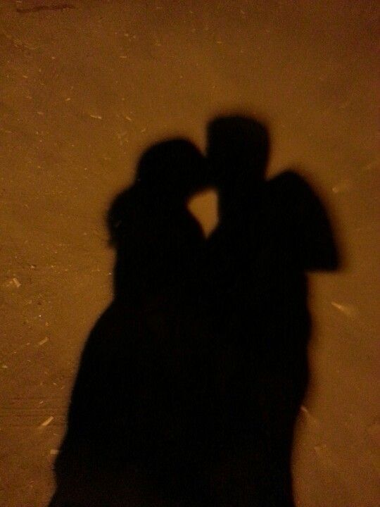 two people standing next to each other in the snow with their shadows on the ground