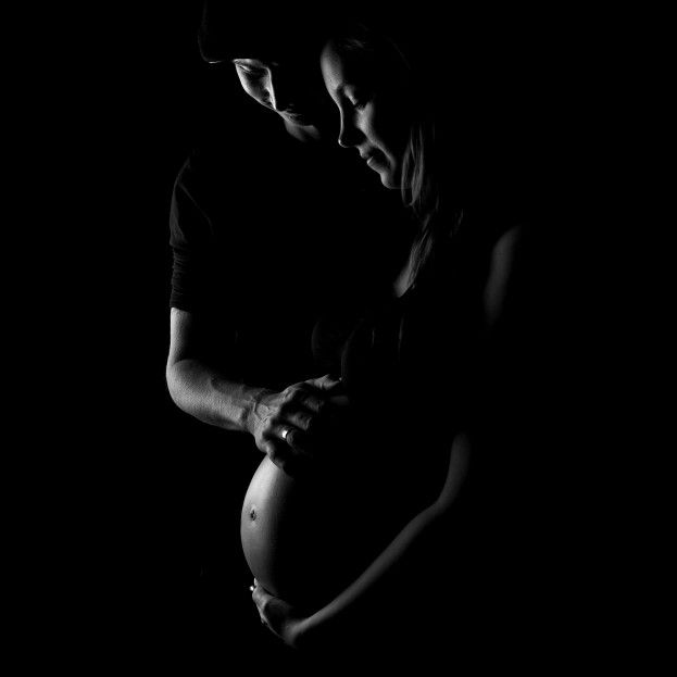 a black and white photo of a pregnant woman holding her baby bump in the dark