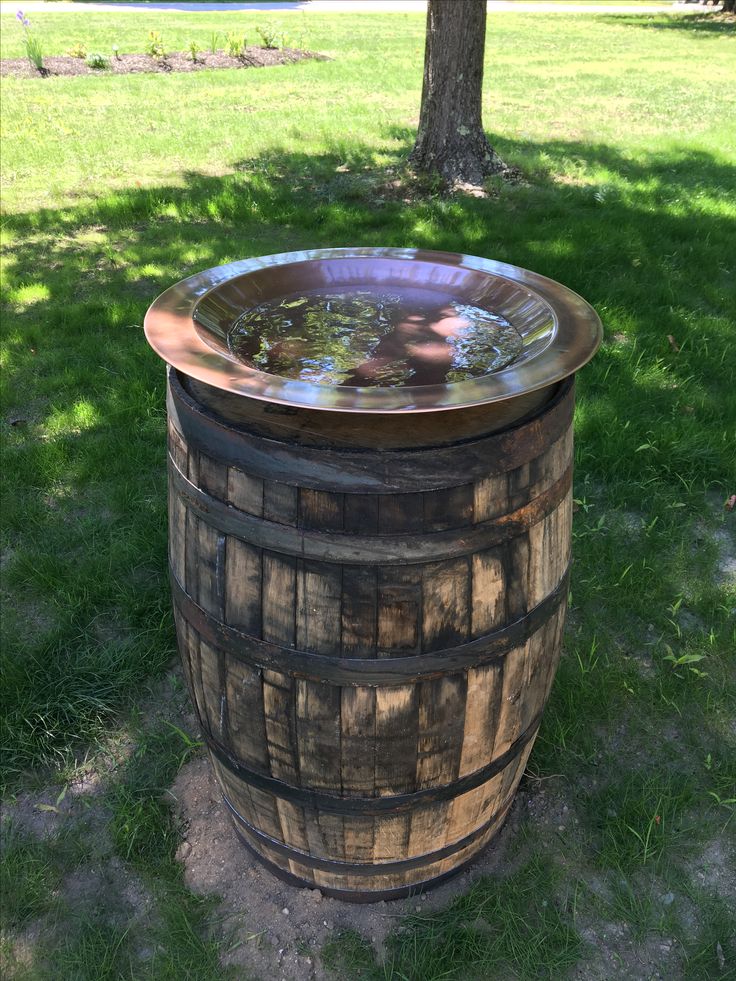 a wooden barrel with water in it sitting on the ground next to a tree and grass