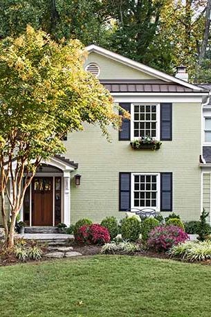 a green house with black shutters and white trim on the front door is shown