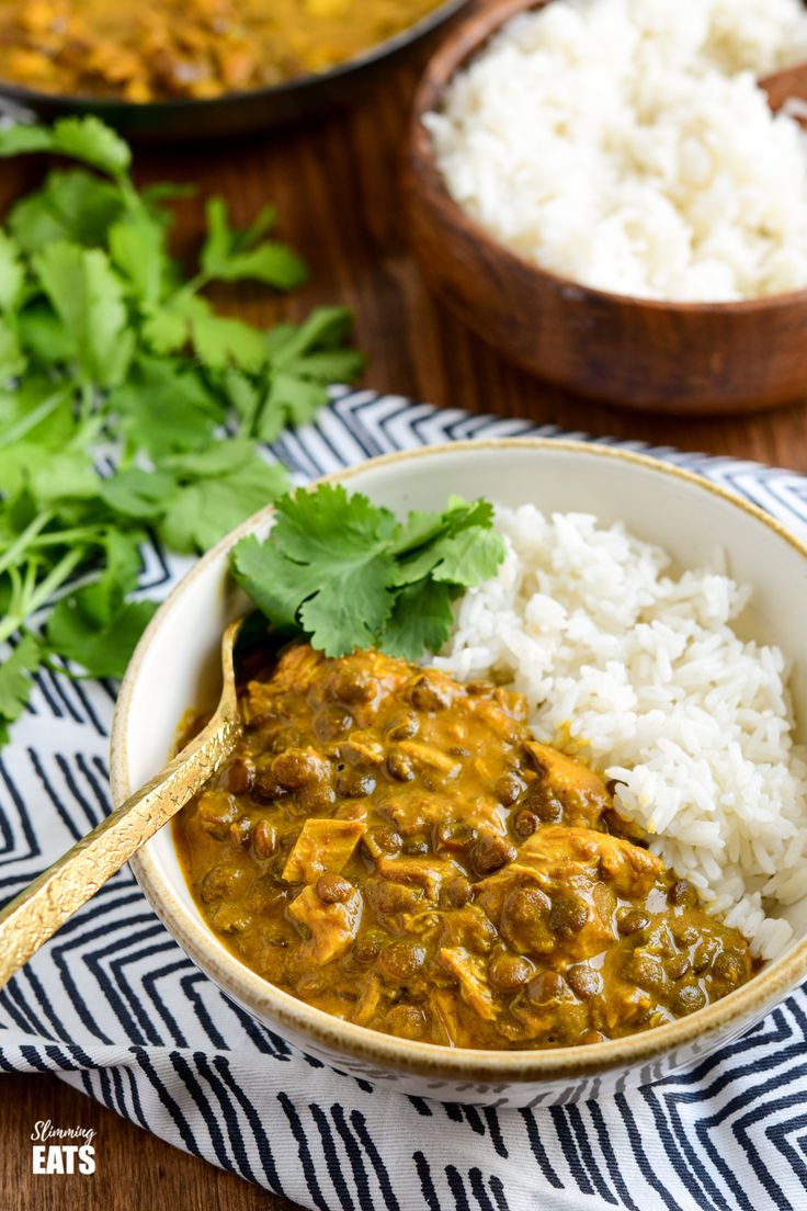 two bowls filled with rice and curry next to some cilantro on a table