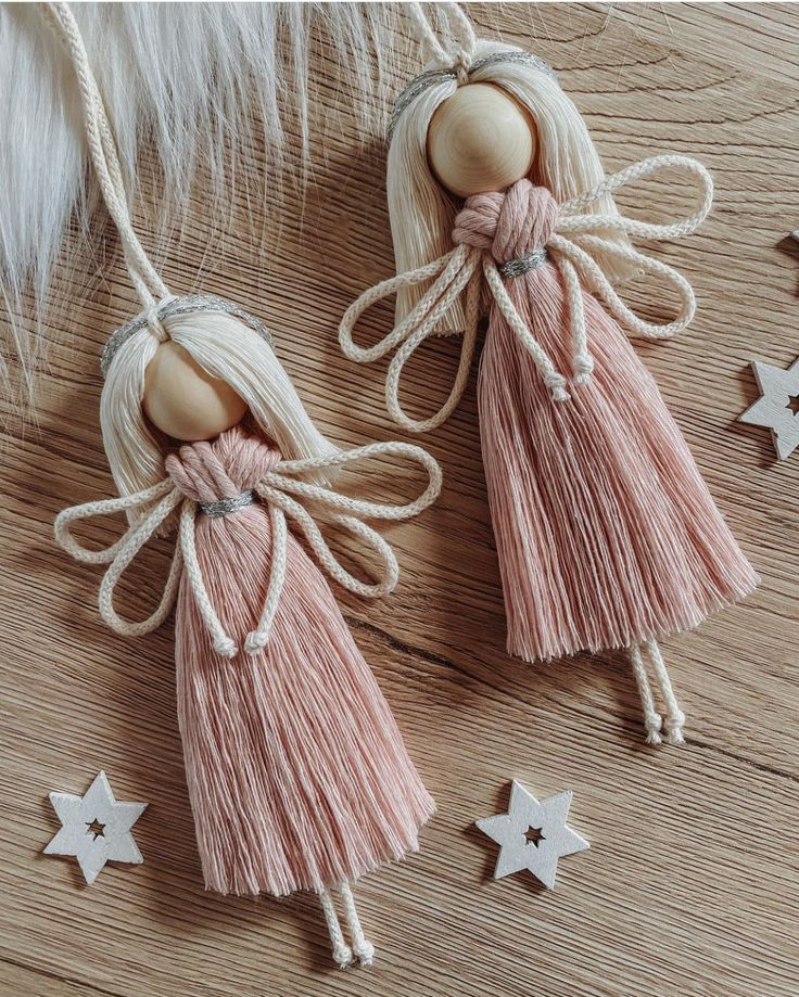 two wooden angel ornaments hanging from strings on a wood floor with stars and feathers in the background