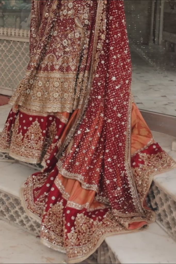 a woman in a red and gold bridal gown standing on steps with her hands behind her head