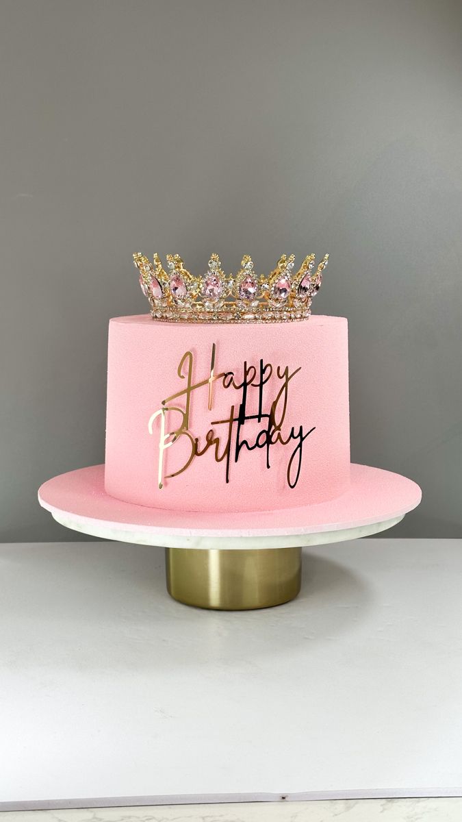 a pink birthday cake with gold crown on top