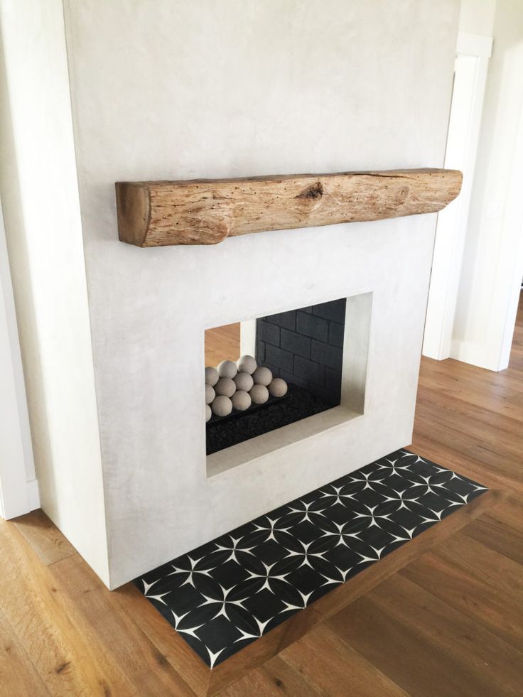 a white fireplace with black and white tiles on the floor next to a wooden mantle