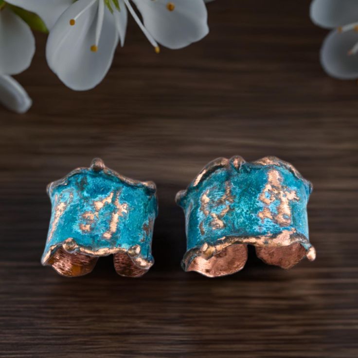 two gold and blue earrings sitting on top of a wooden table next to white flowers