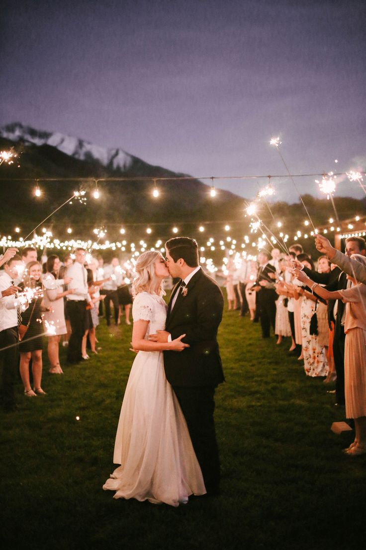 a bride and groom kissing in front of their guests with sparklers on the grass