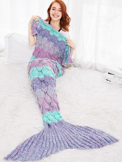 a woman sitting on top of a bed holding up a purple and green mermaid tail blanket