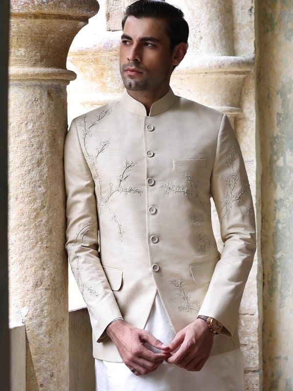 a man in a white suit standing next to pillars and wearing a ring on his finger