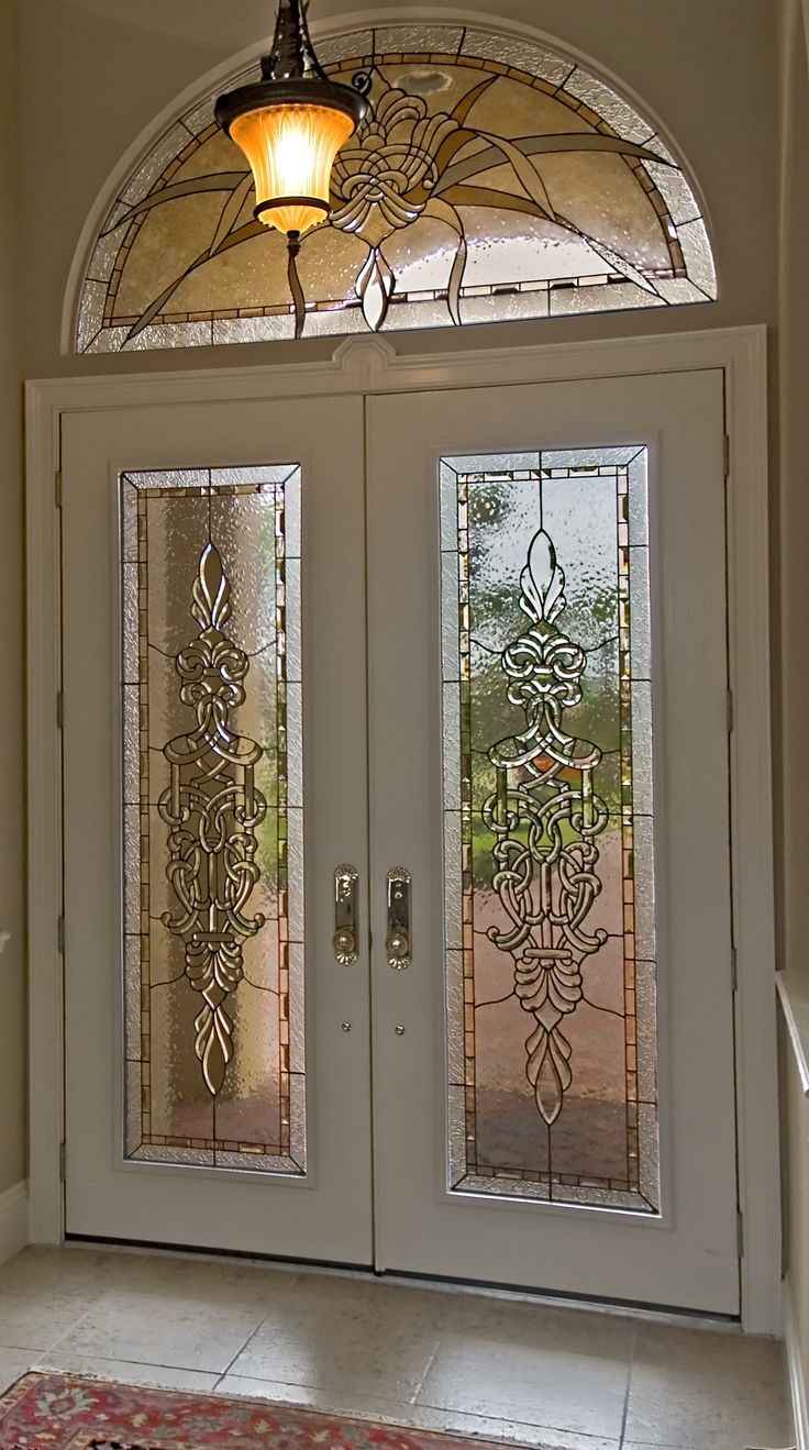 two glass doors with intricate designs on them in front of a light fixture and rug