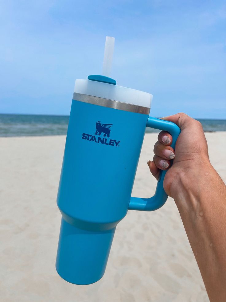 a person holding up a blue cup on the beach