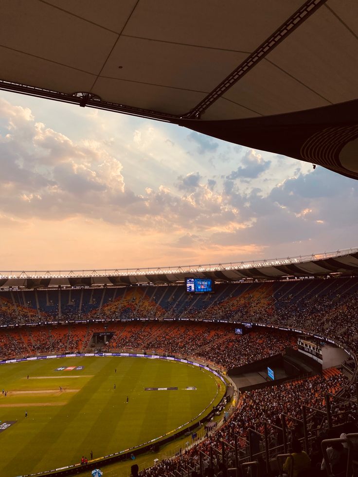 a stadium filled with lots of people watching a baseball game at sunset or sunrise time