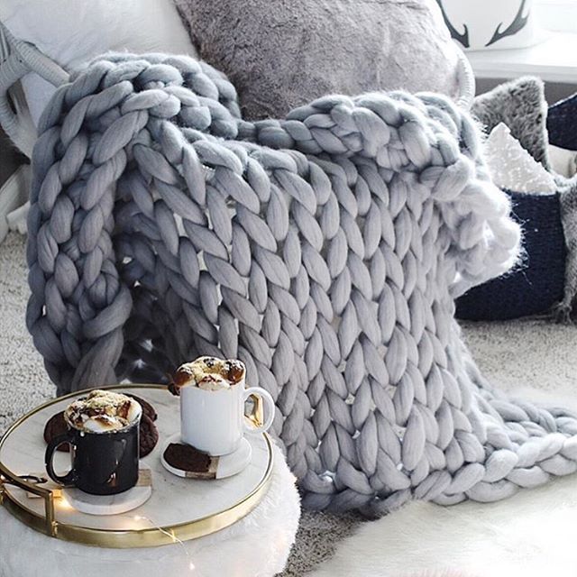 two cups of hot chocolate on a plate next to a knitted blanket and pillows