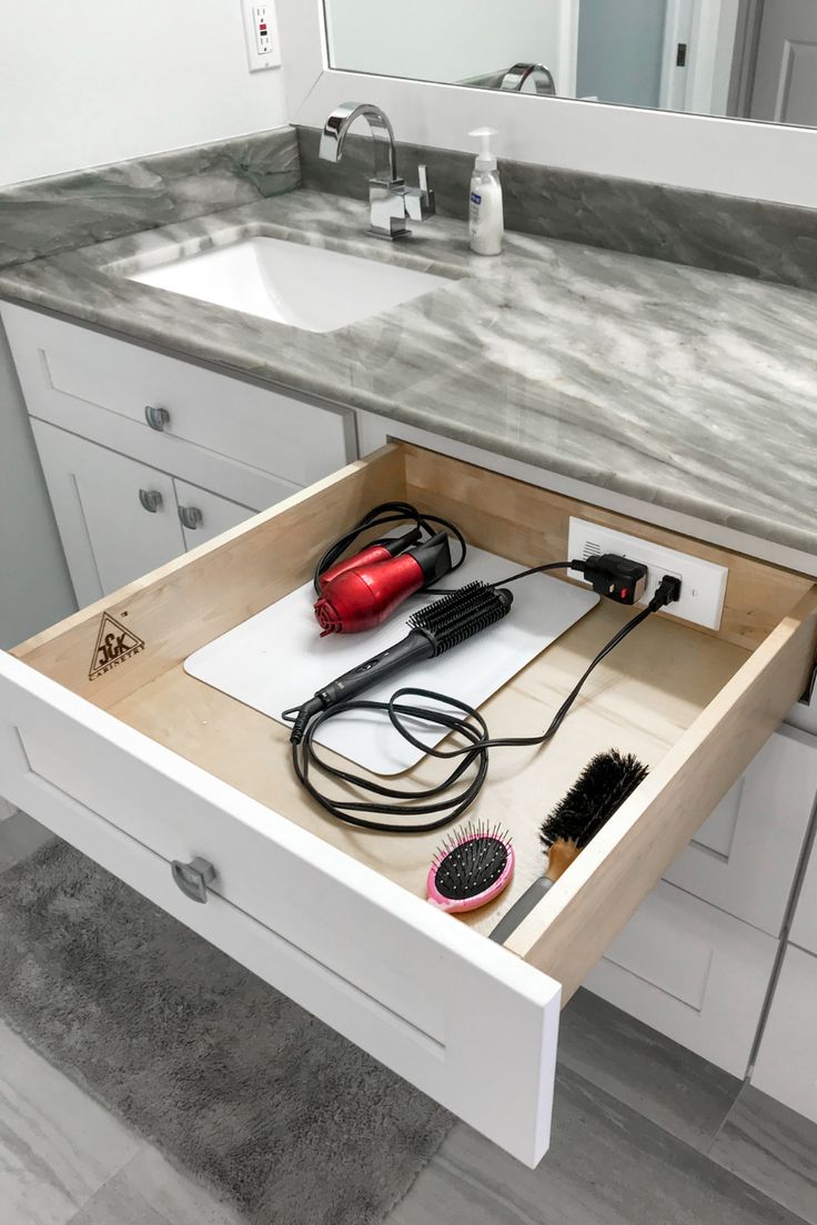 an open drawer in a bathroom with hair dryers and combs on the counter