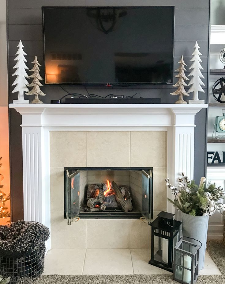 a living room with a fireplace, television and christmas trees on the mantels