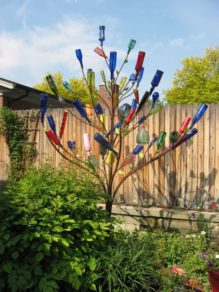 there is a tree made out of glass bottles in the yard with plants around it