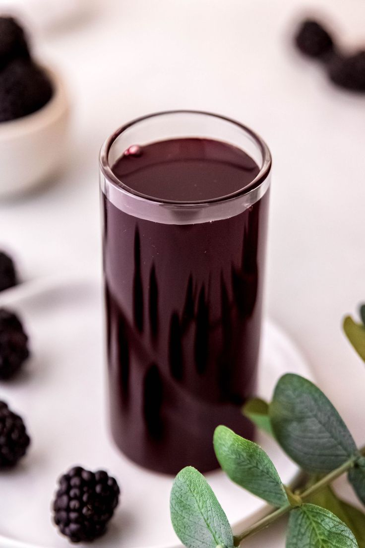 a glass filled with blackberries on top of a white plate next to some leaves