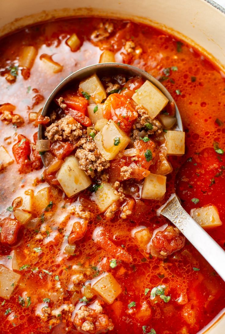 a ladle full of soup with meat and vegetables in it, ready to be eaten