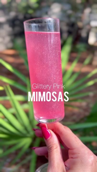 a person holding a glass with pink liquid in it and the words glittery pink mimosa on it