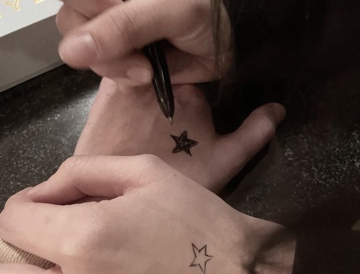 a person with a star tattoo on their left side of her right hand, writing