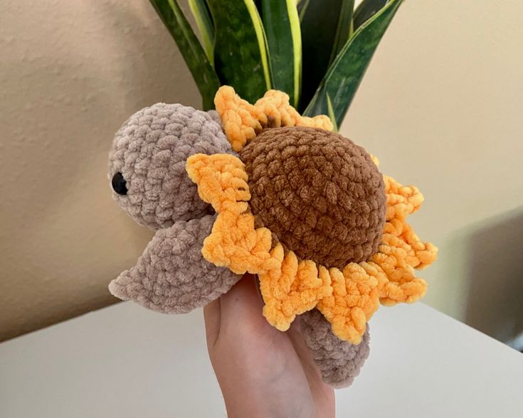 a hand holding a crocheted stuffed animal with a sunflower on it