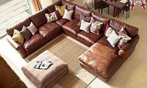 a living room filled with lots of brown couches and pillows on top of a rug