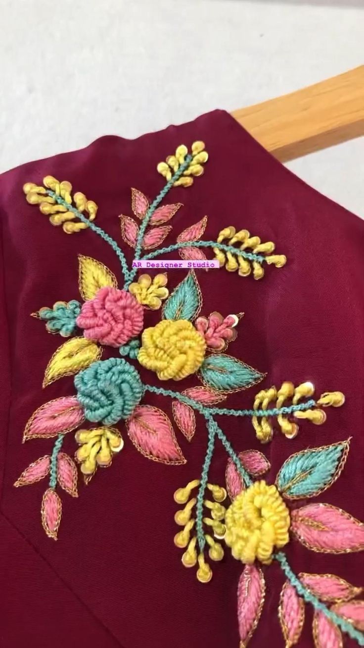 an embroidered jacket with flowers and leaves on the front, sitting next to a piece of wood