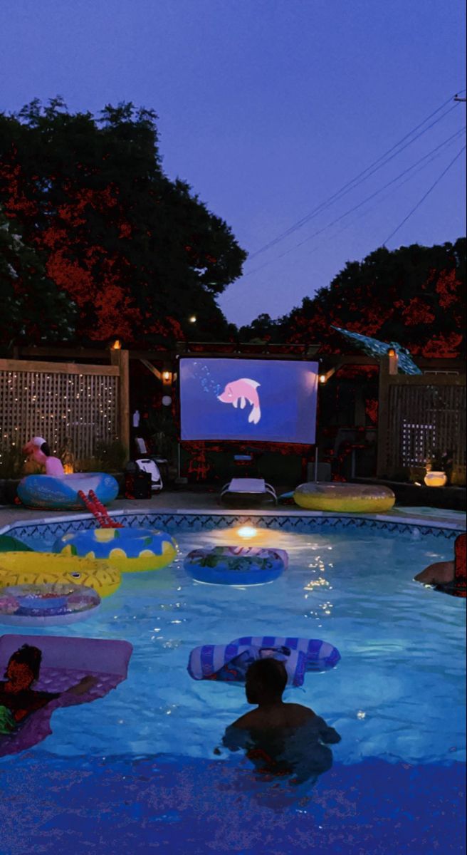 people are in the swimming pool watching a movie at night with an inflatable float