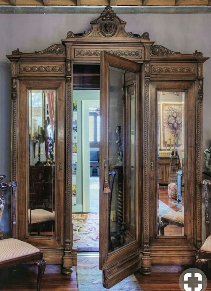 an ornate wooden armoire with mirrored doors in a living room next to a chair