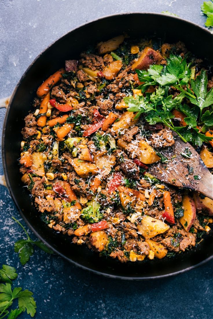 a skillet filled with meat and vegetables on top of a blue counter next to parsley