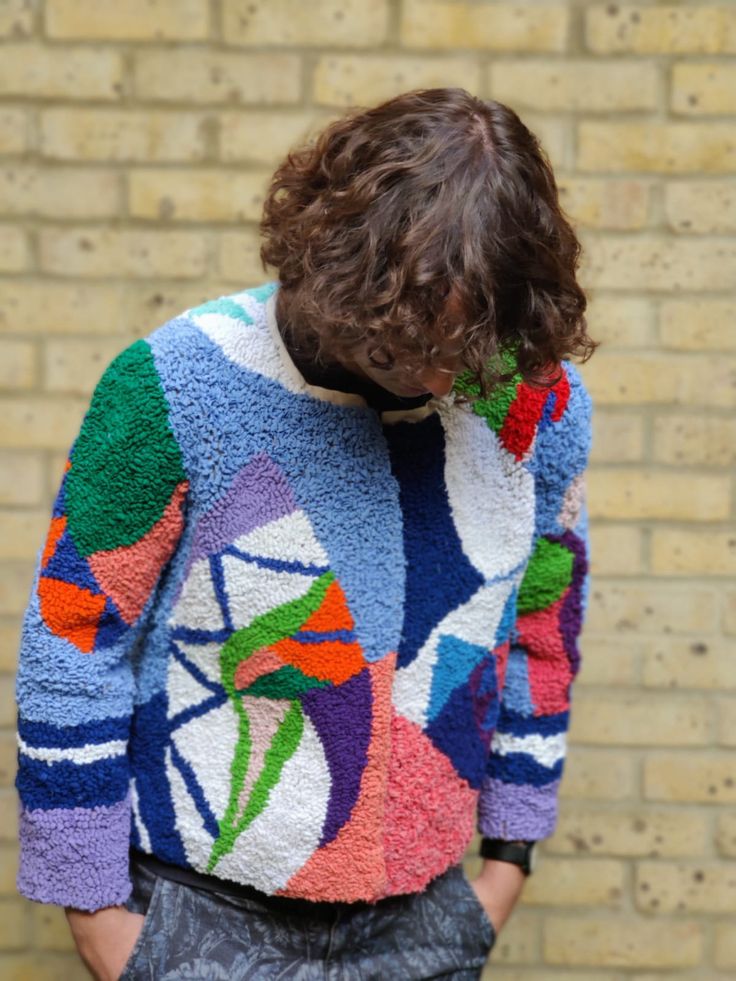 a person standing in front of a brick wall wearing a colorful sweater and black pants