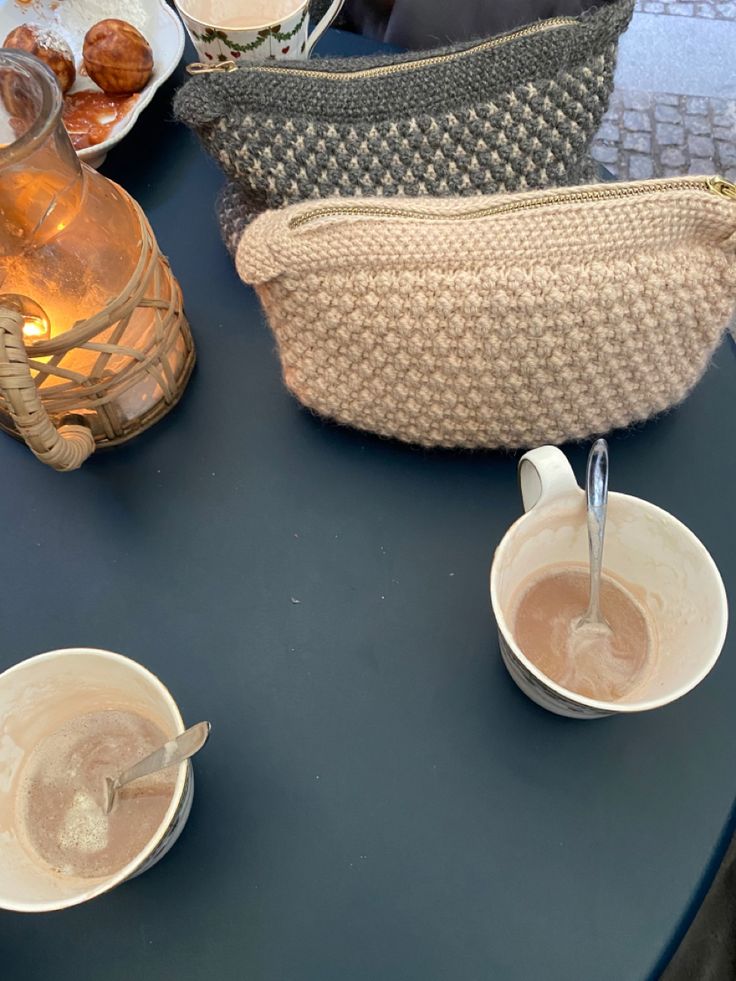 there are two cups on the table with spoons next to it and an empty purse