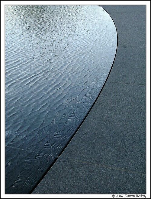 the water is reflecting the sky and its reflection on the pavement in front of it