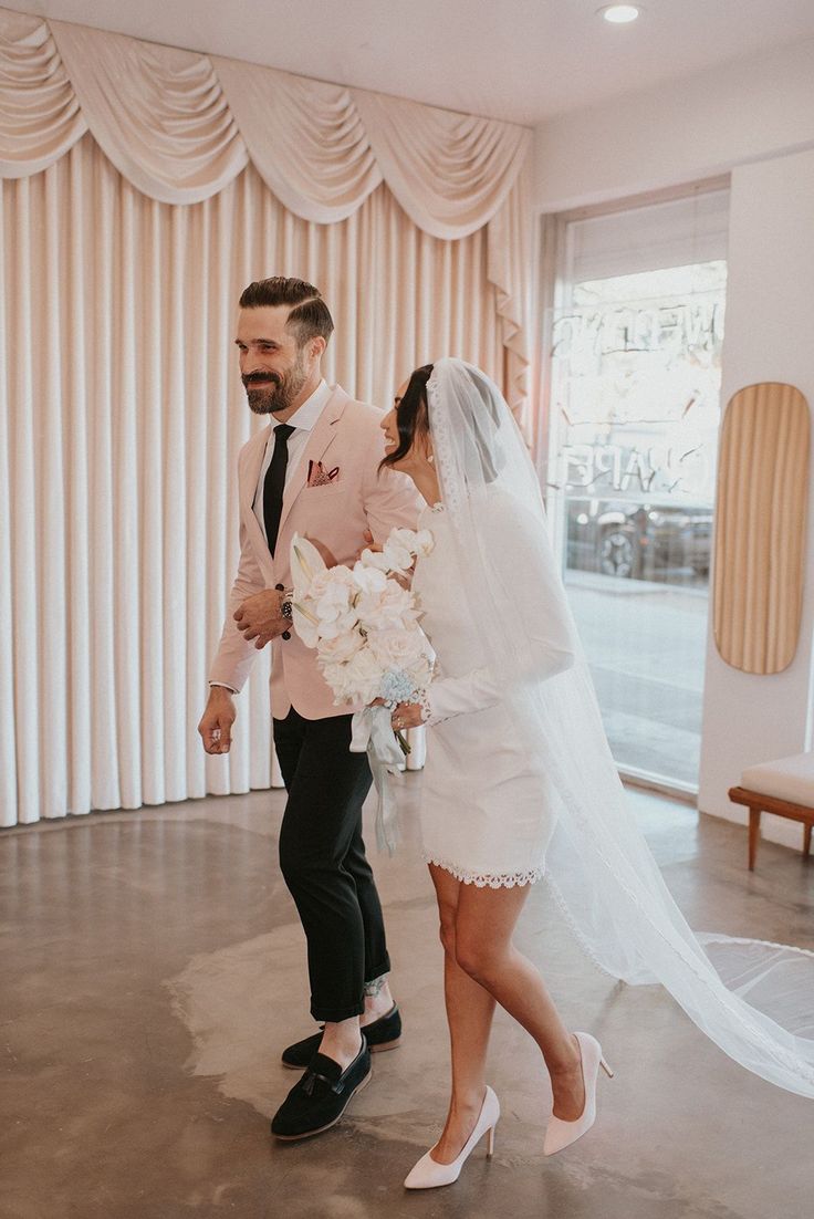 a bride and groom walking down the aisle at their wedding in front of a curtained window