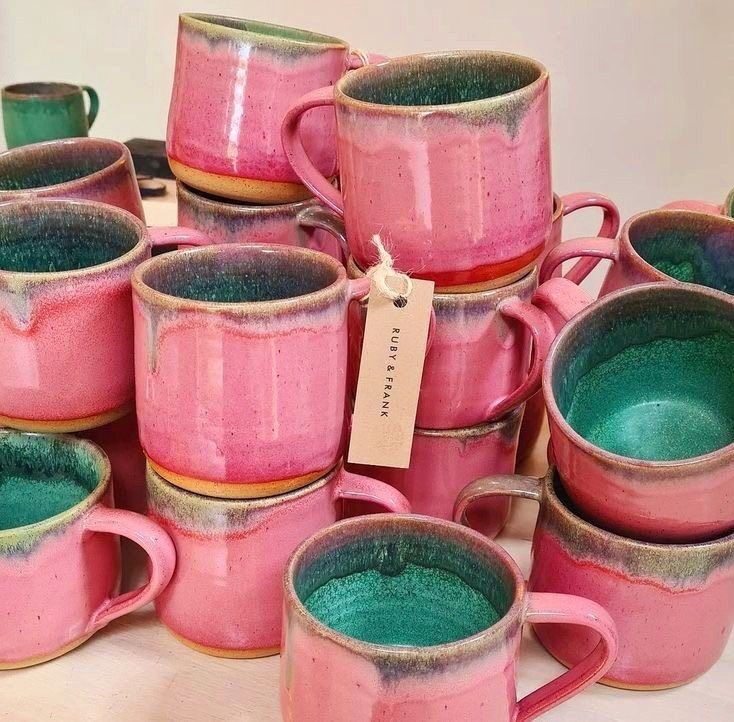 a pile of pink and green coffee mugs sitting next to each other on top of a table