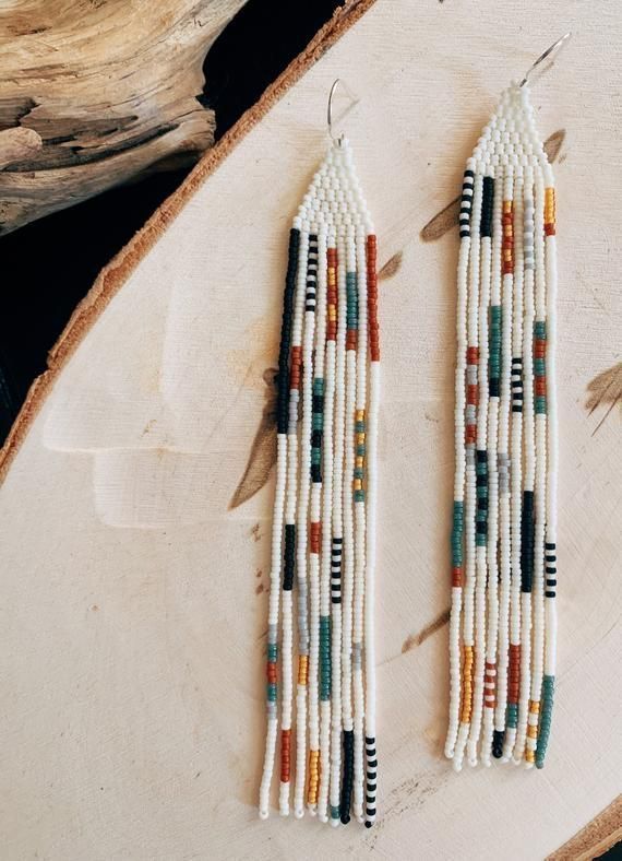 two white and green beaded earrings sitting on top of a piece of wood