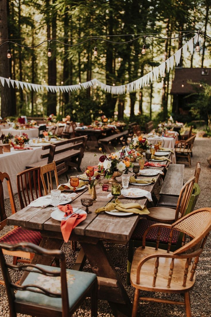 an outdoor table set up with place settings for dinner in the middle of a forest