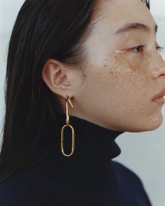 a woman with black hair wearing large gold hoop earrings on her ear and looking off to the side