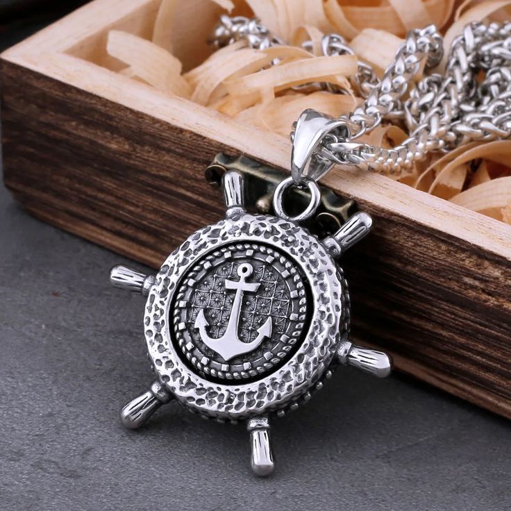 a necklace with an anchor on it and a wooden box in the background that is filled with jewelry