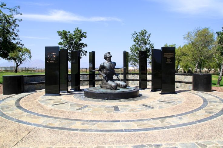 a statue in the middle of a circular area with several black pillars and trees behind it