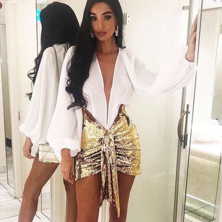 a woman standing in front of a mirror wearing gold sequin shorts and white shirt