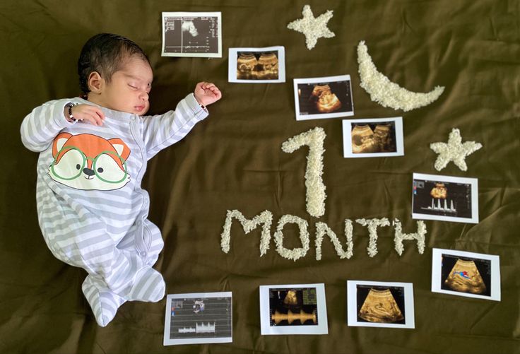 a baby laying on top of a blanket covered in pictures and writing that reads 1 month