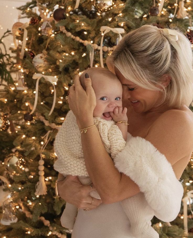 a woman holding a baby in front of a christmas tree