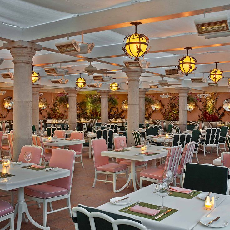 a restaurant with tables and chairs covered in pink and white linens, lit by chandeliers