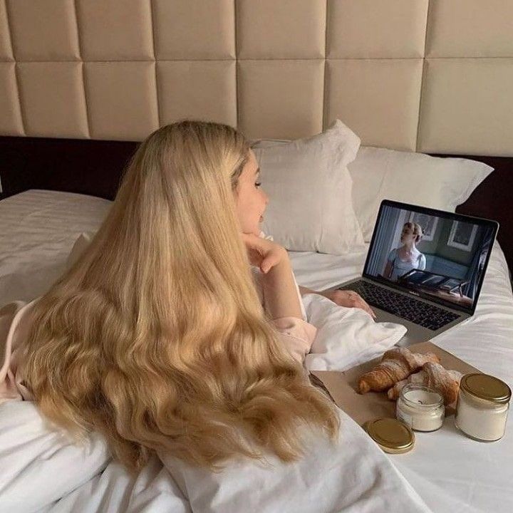 a woman laying in bed with her laptop and food on the table next to her