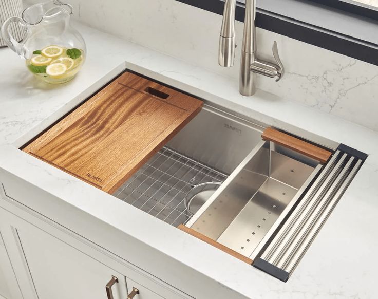 a stainless steel kitchen sink with wooden cutting board in the center and window behind it