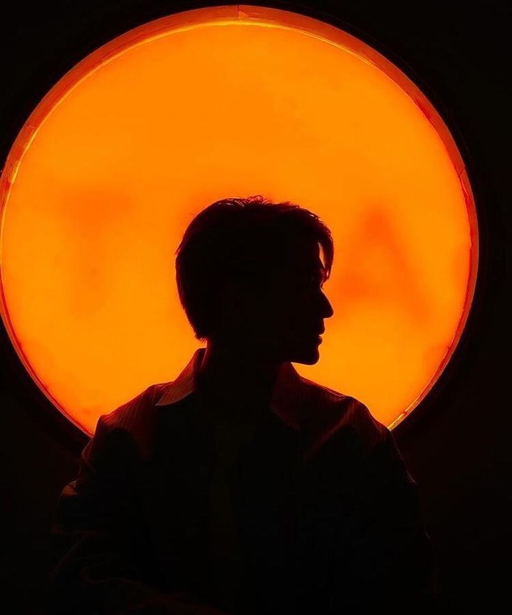 the silhouette of a man in front of an orange light with his head turned to the side