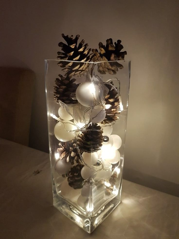 a glass vase filled with pine cones and lights