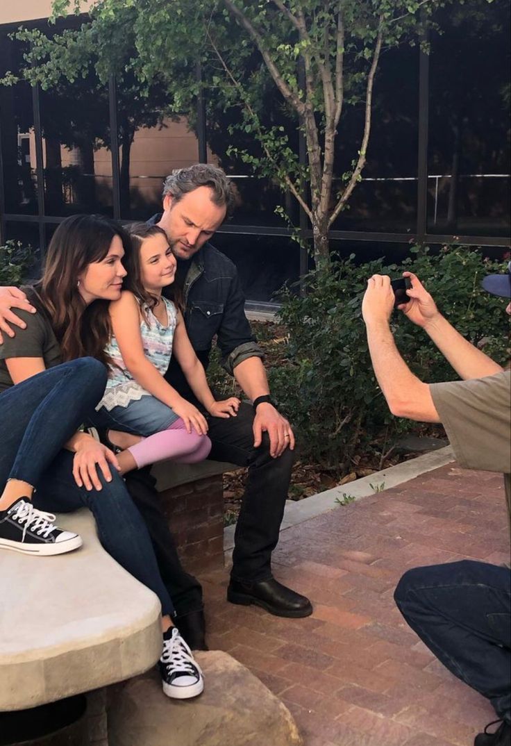 three people sitting on a bench taking pictures with their cell phones while another person takes a photo