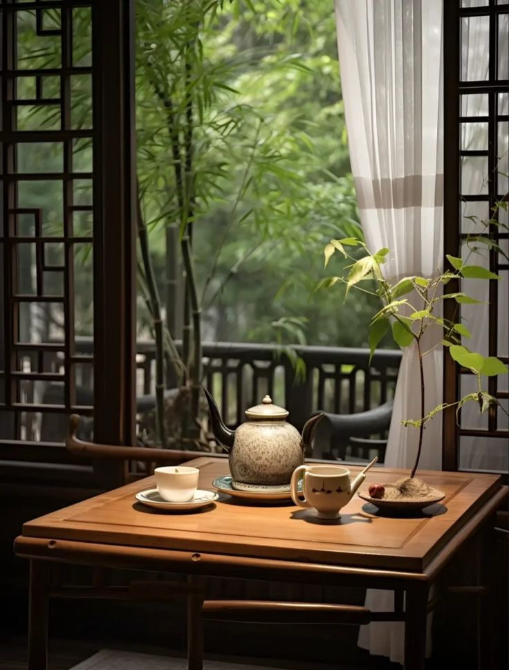 a tea set on a table in front of an open window with bamboo trees outside